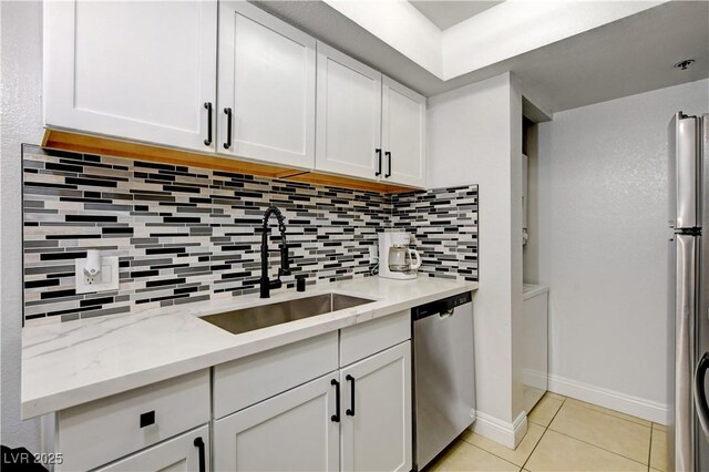 kitchen with appliances with stainless steel finishes, a sink, decorative backsplash, light tile patterned flooring, and white cabinets