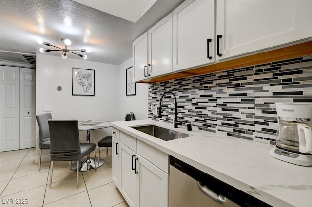 kitchen with a sink, stainless steel dishwasher, light tile patterned floors, decorative backsplash, and white cabinetry