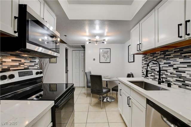 kitchen with stainless steel appliances, a sink, backsplash, light tile patterned floors, and white cabinetry