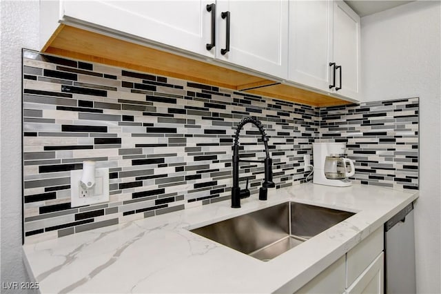 kitchen with a sink, backsplash, white cabinets, stainless steel dishwasher, and light stone counters