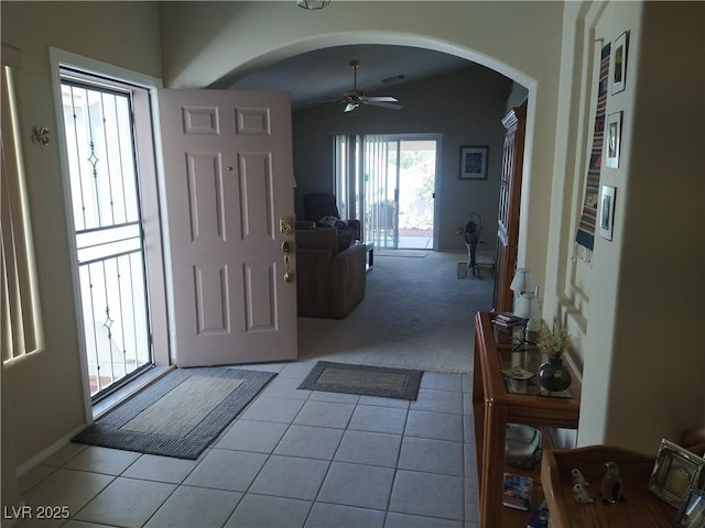 entryway with arched walkways, ceiling fan, light tile patterned floors, and light colored carpet