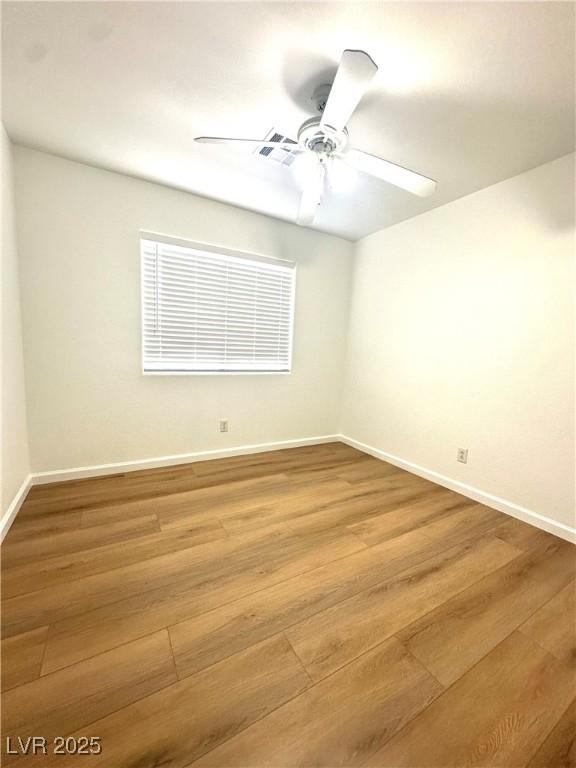 empty room with wood finished floors, a ceiling fan, and baseboards