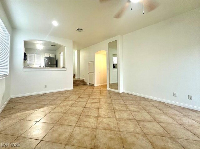 empty room with arched walkways, a ceiling fan, baseboards, and light tile patterned floors