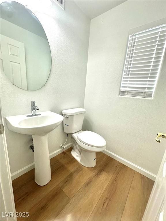 bathroom featuring baseboards, wood finished floors, and toilet