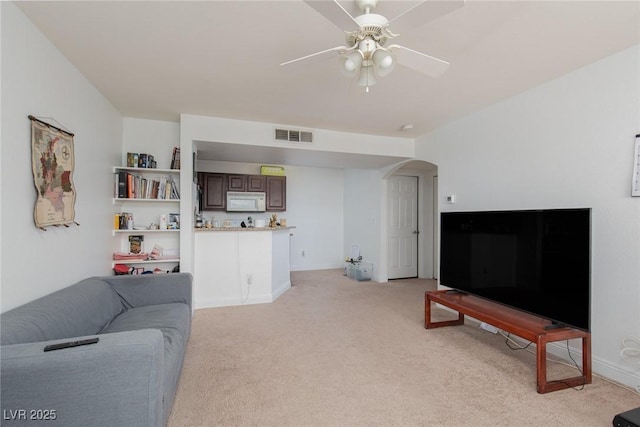 living area featuring light carpet, arched walkways, and a ceiling fan