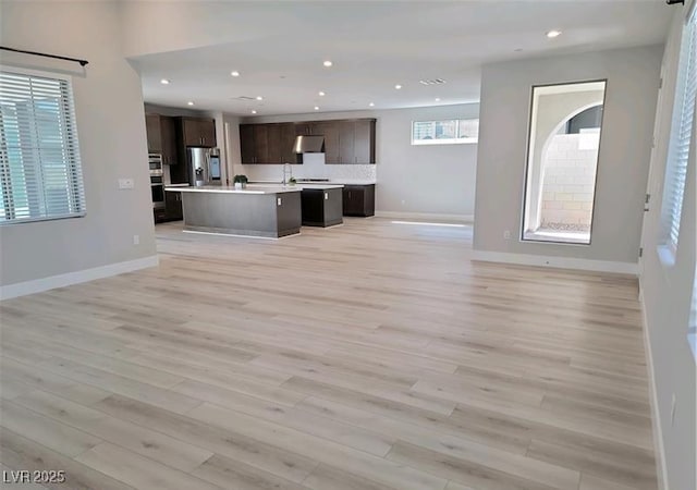 unfurnished living room featuring light wood-style floors, recessed lighting, baseboards, and a sink