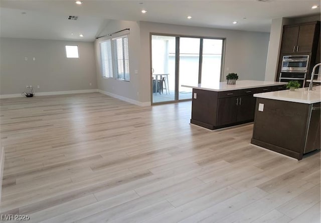kitchen with a kitchen island with sink, light countertops, open floor plan, baseboards, and light wood finished floors