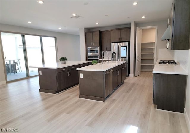 kitchen with a center island with sink, stainless steel appliances, dark brown cabinetry, a sink, and recessed lighting