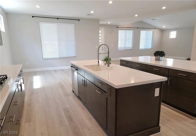 kitchen featuring a sink, a kitchen island with sink, dishwasher, light countertops, and light wood-style floors
