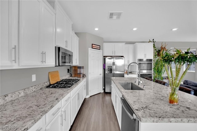 kitchen with appliances with stainless steel finishes, a sink, dark wood-style flooring, an island with sink, and white cabinetry