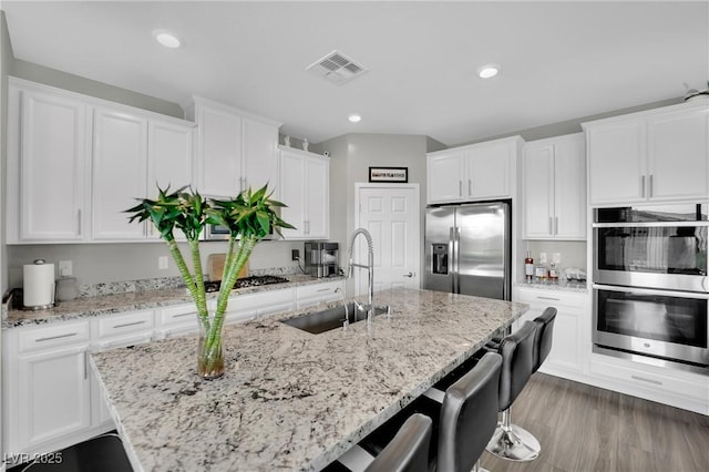 kitchen featuring stainless steel appliances, a sink, an island with sink, white cabinets, and recessed lighting