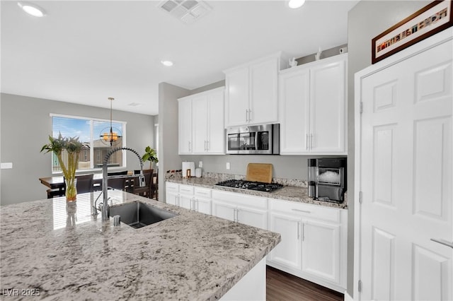 kitchen featuring stainless steel microwave, gas stovetop, a sink, white cabinetry, and recessed lighting