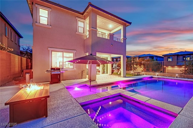 pool at dusk with a fenced backyard, a patio, an outdoor fire pit, and a pool with connected hot tub