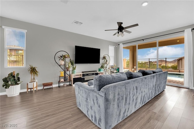 living area featuring healthy amount of natural light, a ceiling fan, wood finished floors, and baseboards