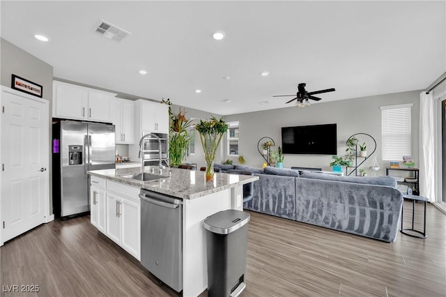 kitchen with stainless steel appliances, a sink, ceiling fan, a center island with sink, and white cabinetry