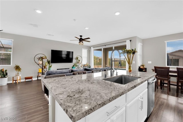 kitchen with a sink, a ceiling fan, dark wood finished floors, a center island with sink, and light stone countertops
