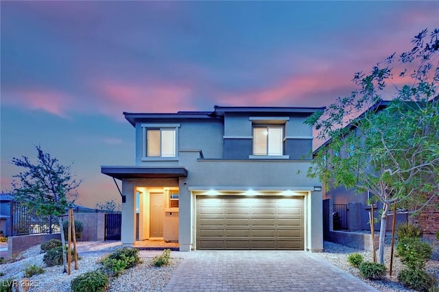 view of front of house featuring stucco siding, fence, a garage, and decorative driveway