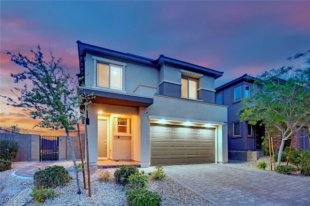 view of front of home featuring stucco siding, an attached garage, decorative driveway, and a gate