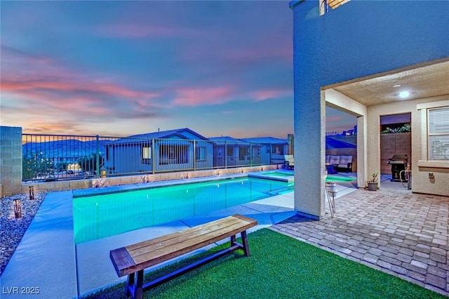 pool at dusk featuring a patio area, grilling area, and a pool with connected hot tub