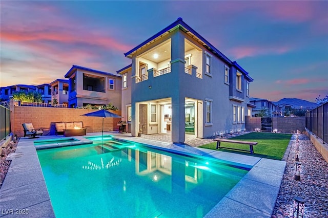 back of house at dusk featuring a balcony, a fenced backyard, a patio, and stucco siding