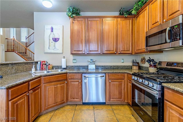 kitchen featuring appliances with stainless steel finishes, a sink, light tile patterned floors, and brown cabinets