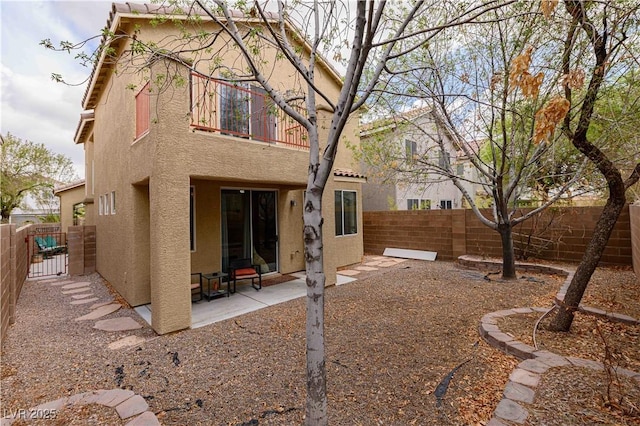 rear view of property with stucco siding, a fenced backyard, a patio, and a gate