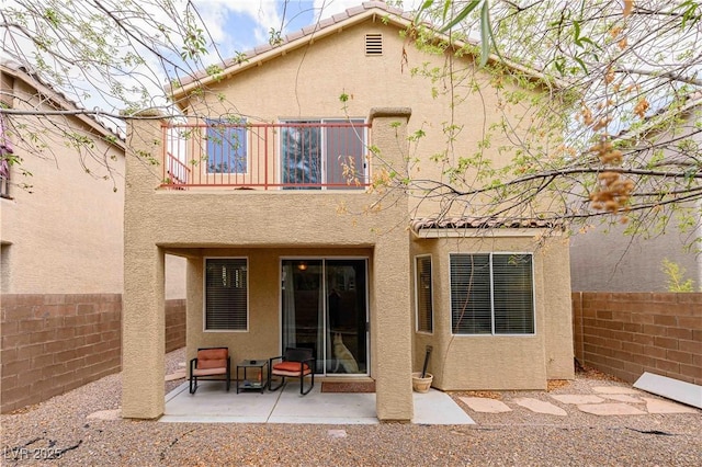 rear view of house featuring stucco siding, a balcony, a fenced backyard, and a patio