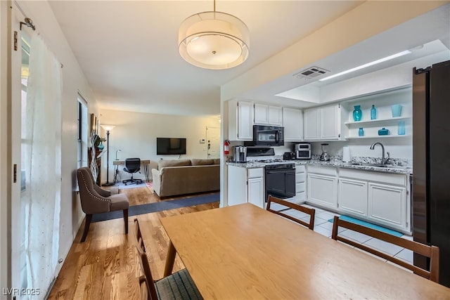 5576 W Rochelle Ave Unit 27C, Las Vegas, NV 89103 - kitchen with range with gas stovetop, black microwave, a sink, white cabinetry, and open shelves