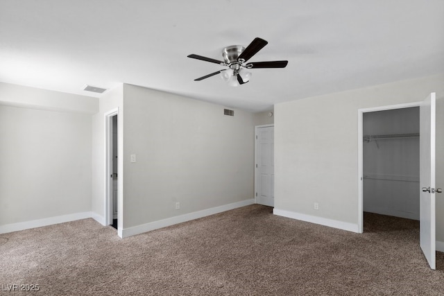 unfurnished bedroom with carpet, a walk in closet, a closet, and a ceiling fan