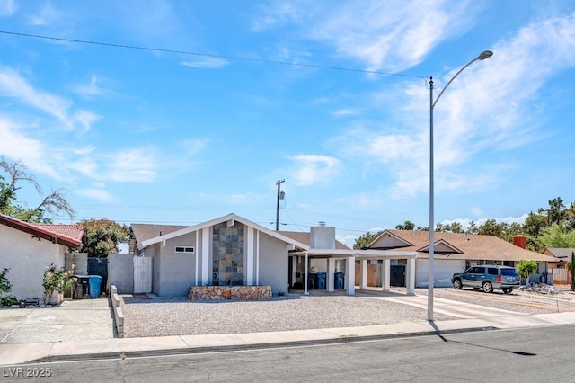 mid-century inspired home with driveway, stucco siding, a chimney, fence, and stone siding