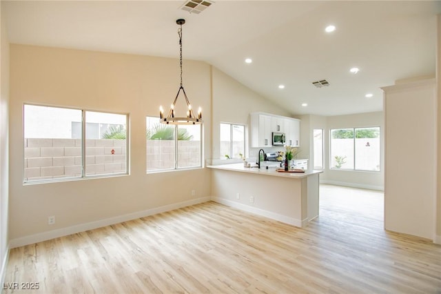 kitchen with a chandelier, light wood-style floors, appliances with stainless steel finishes, white cabinets, and lofted ceiling