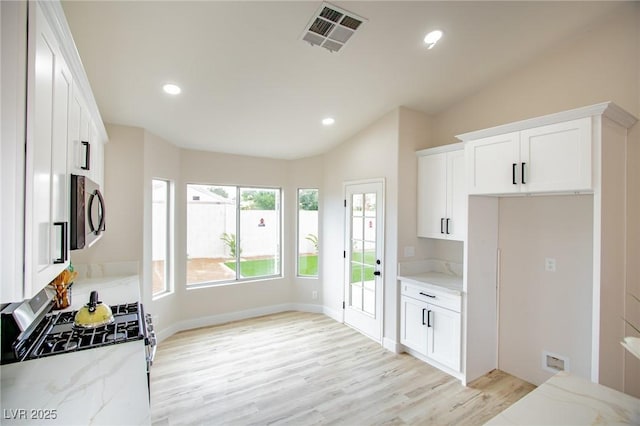 kitchen featuring stainless steel appliances, light stone countertops, light wood-style flooring, vaulted ceiling, and white cabinetry