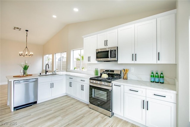 kitchen featuring stainless steel appliances, a sink, a chandelier, light wood-style floors, and a peninsula