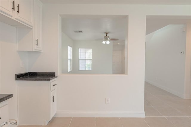 kitchen featuring dark countertops, ceiling fan, light tile patterned floors, and white cabinetry