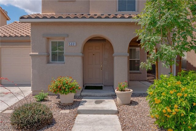 view of exterior entry featuring a garage, stucco siding, a tile roof, and concrete driveway