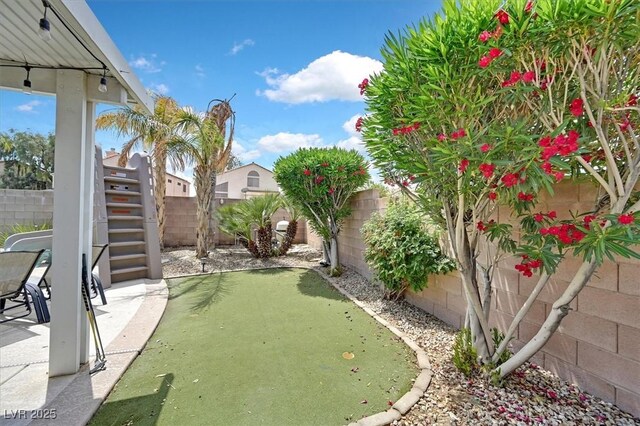 fenced backyard featuring stairs, a putting area, and a patio