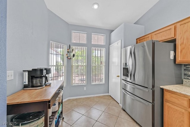 kitchen with stainless steel refrigerator with ice dispenser, light tile patterned floors, light brown cabinetry, baseboards, and light stone countertops