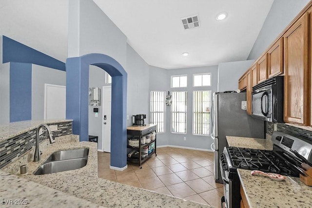 kitchen with stainless steel gas range oven, a sink, black microwave, light tile patterned floors, and arched walkways