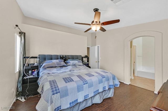 bedroom with arched walkways, wood finished floors, baseboards, a ceiling fan, and ensuite bath