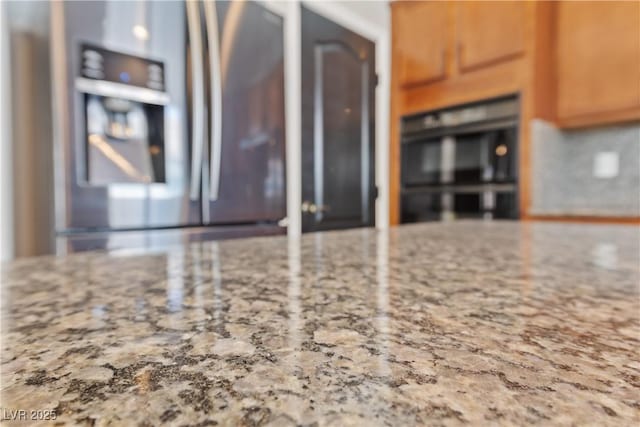 kitchen with stainless steel refrigerator with ice dispenser, double oven, light stone counters, and brown cabinets