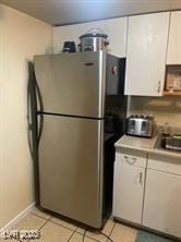 kitchen featuring freestanding refrigerator, white cabinetry, light countertops, light tile patterned floors, and a sink