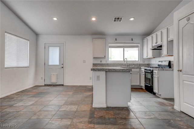 kitchen featuring black gas range oven, under cabinet range hood, stone tile flooring, baseboards, and recessed lighting