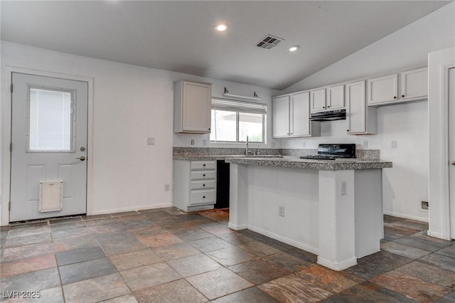 kitchen with under cabinet range hood, stove, baseboards, stone tile floors, and vaulted ceiling