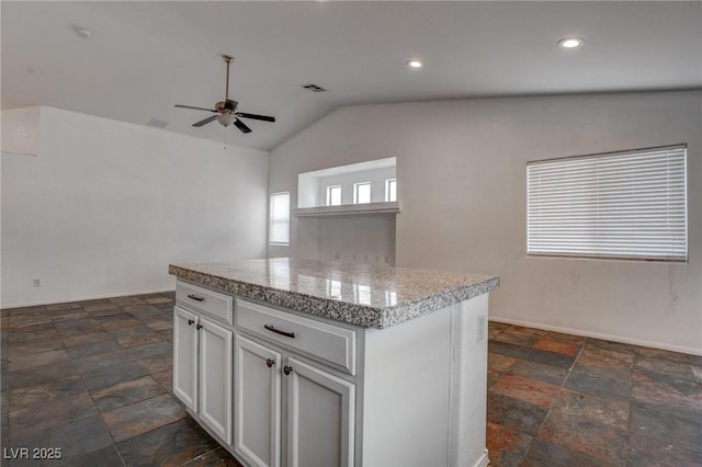 kitchen with stone tile flooring, ceiling fan, lofted ceiling, a center island, and white cabinetry