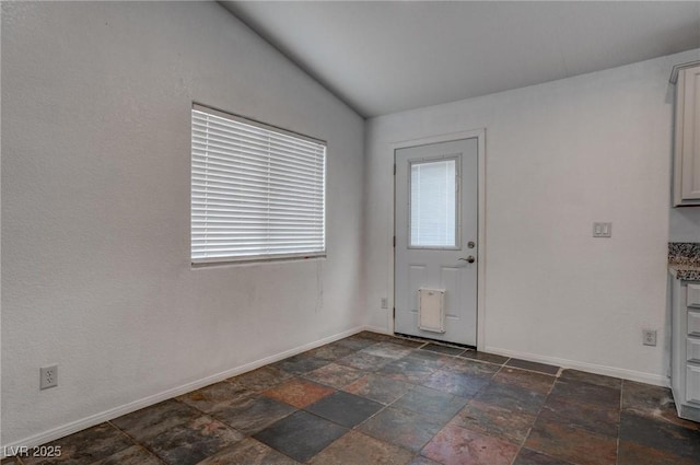 foyer entrance featuring stone tile floors, baseboards, and vaulted ceiling