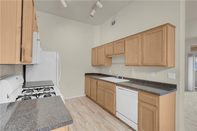 kitchen with white appliances, a sink, dark countertops, light brown cabinets, and baseboards