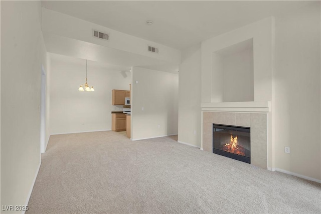 unfurnished living room featuring a tile fireplace, light colored carpet, a chandelier, and baseboards