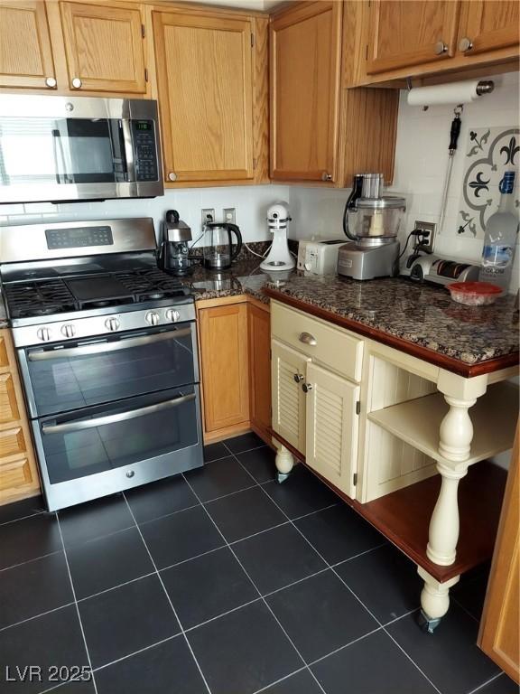 kitchen with stainless steel appliances, dark tile patterned flooring, and dark stone countertops