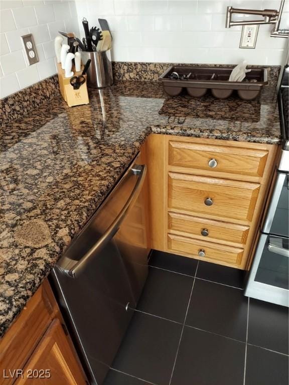 kitchen view of dishwasher, backsplash, brown cabinets, pot filler, and dark stone counters