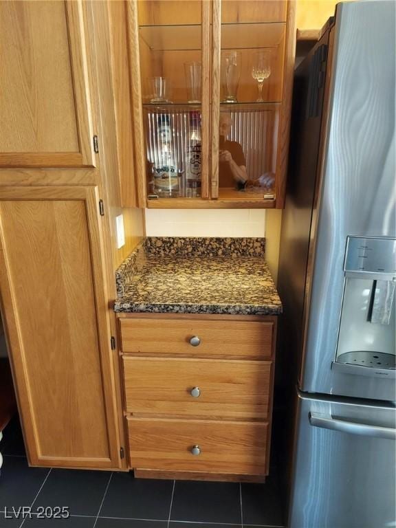 kitchen view of stainless steel refrigerator with ice dispenser, dark stone counters, and brown cabinets